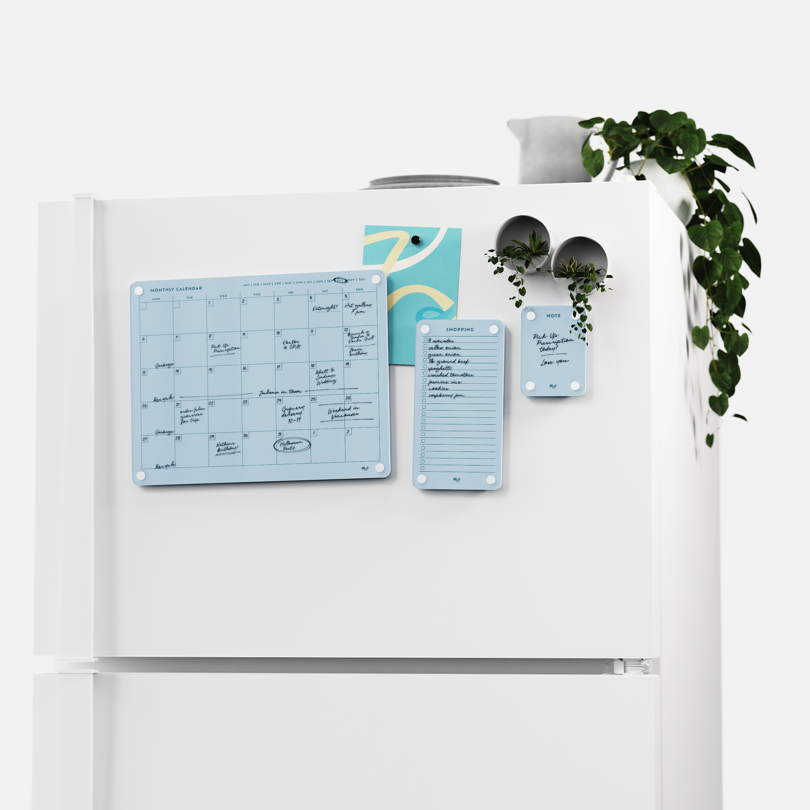 White fridge with the Vista blue monthly calendar, shopping list and note board set, plants on top